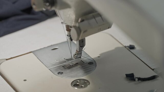 Close up of industrial sewing machine stitching dark fabric while hands guide material