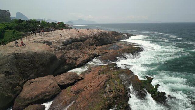 Right aerial orbit over Arpoador rock at Ipanema beach during a cloudy afternoon looking towards rock and city buildings. Recorded in 4K Apple ProRes 422.