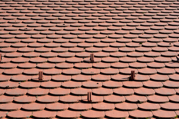 Fototapeta premium A high angle view of red clay roof tiles arranged in a scale pattern featuring small metal snow guards