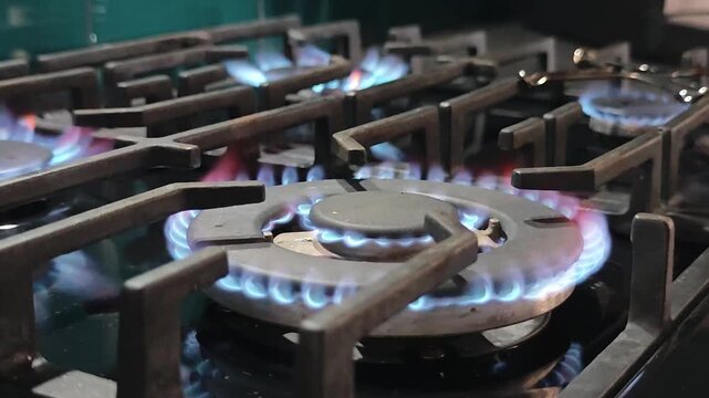 Natural gas burners igniting on modern kitchen stove with blue flames forming circular heat pattern across metal cooktop for energy supply, cooking process and household gas usage concept