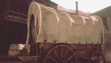 A weathered covered wagon stands prominently in a dusty old town. The sun sets, casting a warm glow on the scene, highlighting the rustic charm and history of the setting. © icetray