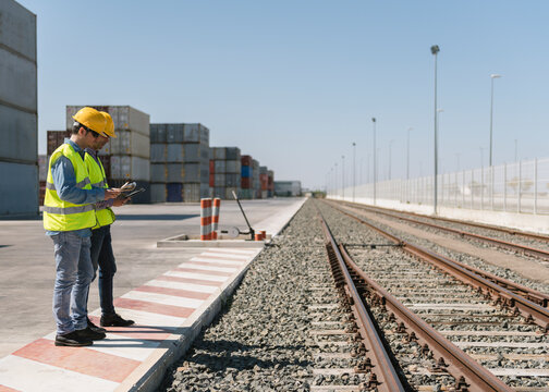 Workers in front of cargo containers near railway tracks on industrial site