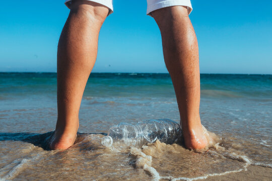 Man's legs and empty plastic bottle at seashore