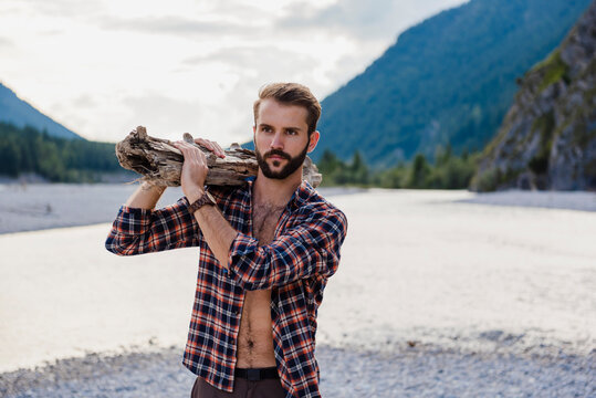 Germany, Bavaria, portrait of young man carrying firewood on his shoulder in nature