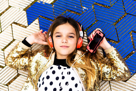 Portrait of girl wearing golden sequin jacket listening music with headphones and smartphone