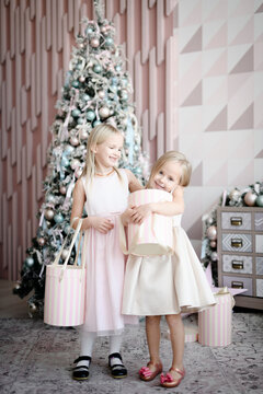 Portrait of two happy little girls standing in front of lighted Christmas tree with gift boxes
