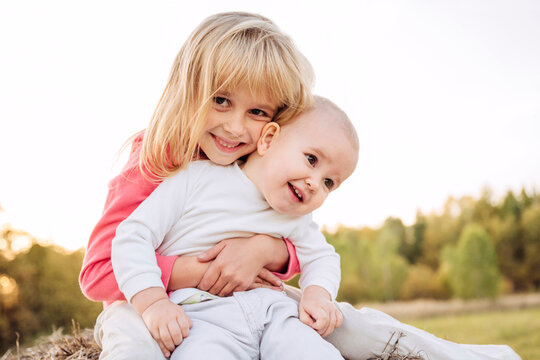 Sister embracing female toddler against clear sky