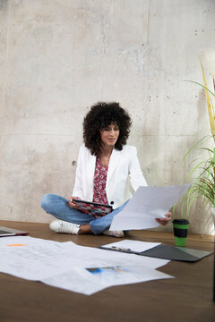 Businesswoman sitting on the floor in a loft working with tablet and documents