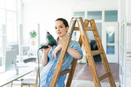 Portrait of woman at ladder holding electric drill