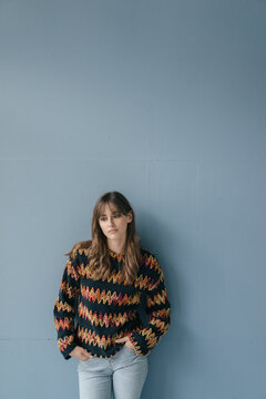 Sad young woman leaning against wall, with hands in pockets