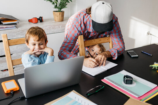 Father writing in notebook while children are playing at his desk