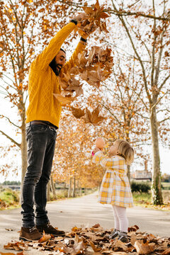 Father and daughter enjoying a morning day in the park in autumn, throwing autumn leaves