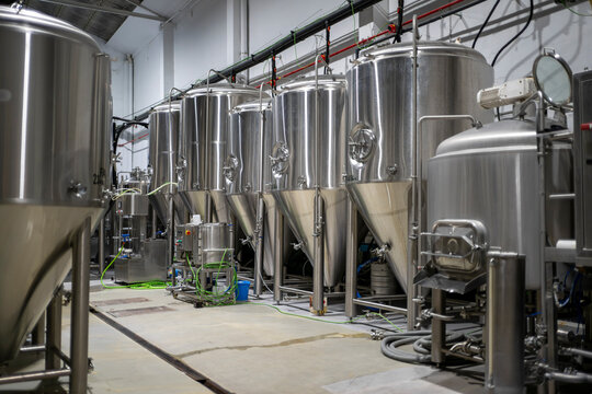 Large stainless steel fermentation tanks aligned inside modern industrial brewery facility with brewing pipelines and production equipment in professional beer manufacturing plant
