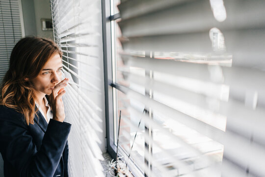 Woman standing by window, spying through blinds