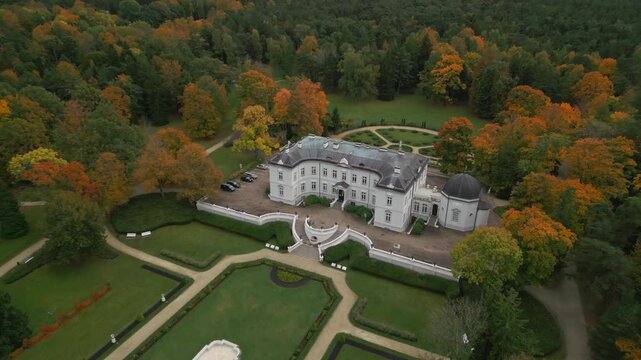 Autumn foliage frames a stately manor house and formal gardens, showcasing a picturesque landscape from an aerial perspective.