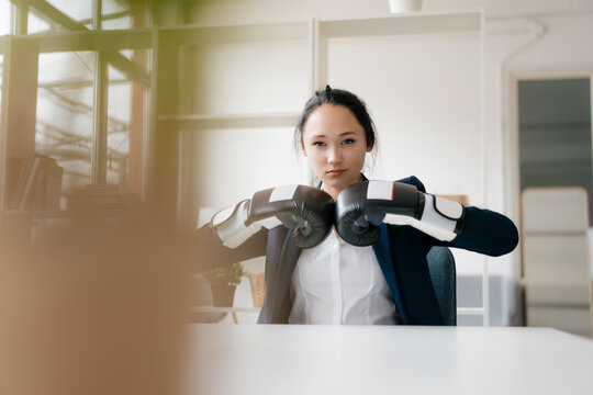 Portrait of young businesswoman sitting at desk wearing boxing gloves