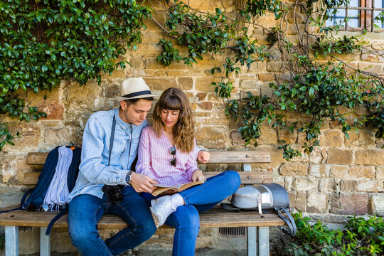 Young couple on a city break, sitting on a bench, reading guidebook