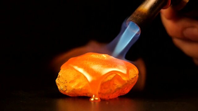 Melting metal with a torch creates a glowing liquid transformation in a dark setting.