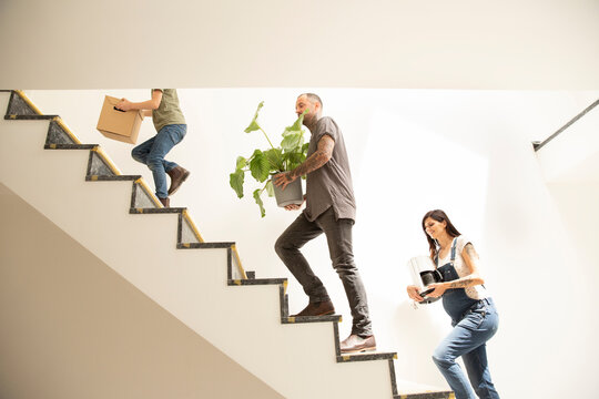 Family carrying various objects while moving up on steps in new apartment