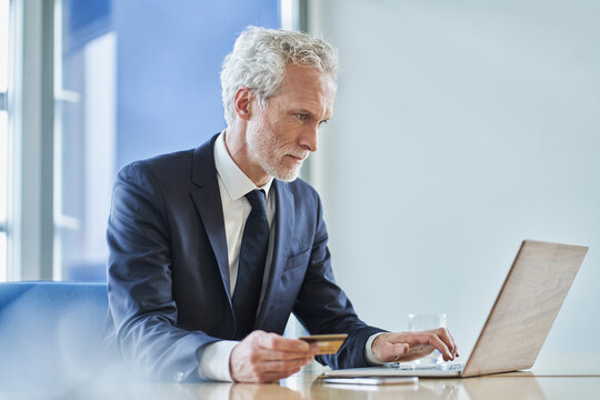 Businessman holding credit card and using laptop at desk in office