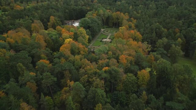 An aerial view of a forest in autumn shows vibrant fall foliage surrounding a formal garden and buildings.