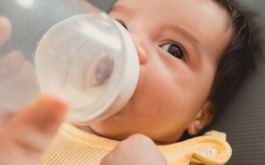 Naklejka premium Close up of baby drinking milk from a feeding bottle, concept of infant nutrition, newborn care and baby feeding.