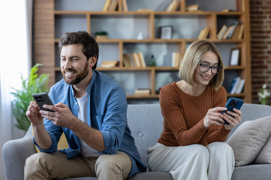 Couple sitting on a sofa in the living room, a man and a woman ignoring each other while engrossed in their individual smartphones, representing phubbing and technology addiction