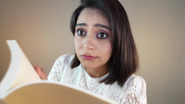 Close up of confused Asian student girl or young woman holding book look at camera feels confusion doubt, isolated over grey studio background.