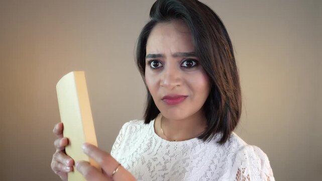 Close up of shocked amazed Asian student girl or young woman holding a book look staring at camera surprisingly feels confusion doubt, isolated over grey studio background.
