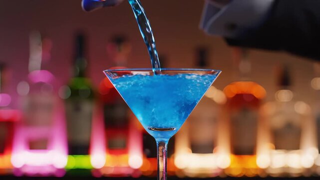 The bartender skillfully pours a bright blue cocktail into a stylish martini glass, sparkling droplets flying through the air.