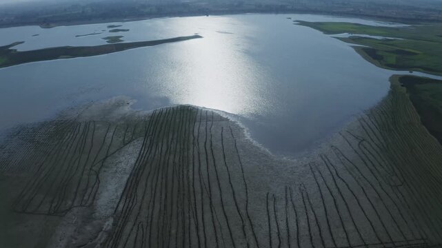 Drone tilts up from spillway to reveal expansive Banas Dam reservoir in Sirohi district, Rajasthan, with calm waters, green shores, and islands under overcast sky.