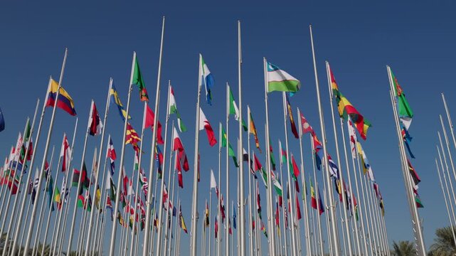 Many international flags waving on tall flagpoles under clear blue sky. Symbol of global cooperation, diplomacy, international relations and unity between countries in modern world.