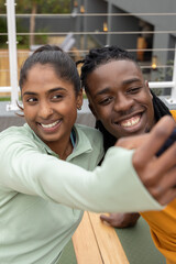 Diverse couple posing and leaning close on rooftop patio, holding smartphone on wooden bench © wavebreak3
