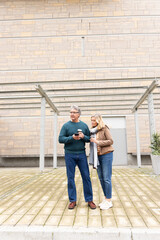 Senior and middle-aged couple standing on paved plaza holding coffee cups and checking smartphone © wavebreak3