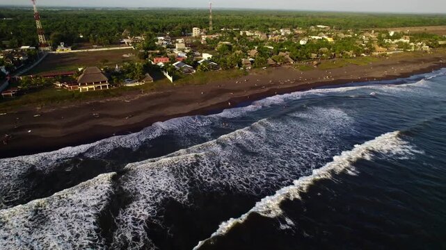 Aerial zoom in revealing a coastal village and black sand beach in Tenerife with waves breaking along the Atlantic shoreline.