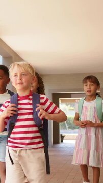 Vertical video: Walking forward blond boy in striped tee leading peers with packs at school to exit
