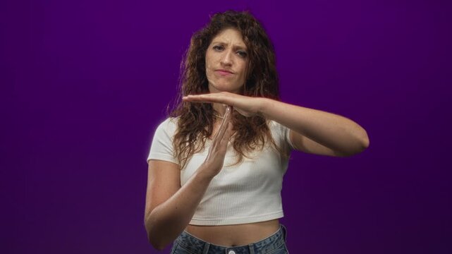 Woman showing hands making timeout gesture with palms visible, wearing white crop top and jeans in purple studio; frustration refusal.