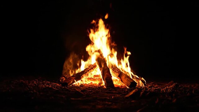 Campfire burns brightly at night, radiating fire, warmth, and light in the darkness. Logs ignite in a vibrant outdoor setting.