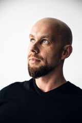 Fototapeta premium Man with a bald head and beard looks up in a simple indoor space in the daytime