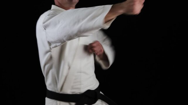 A professional male athlete in karate practices punches and blocks with his hands at a high pace on a black background