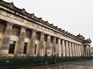 Naklejka premium Historic neoclassical National Gallery building with grand stone columns and ornate facade in Edinburgh, Scotland, UK on a rainy city street