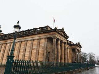 Naklejka premium Neoclassical National Gallery museum facade with sandstone columns, iron railings and flags in Edinburgh, Scotland, UK on an overcast rainy day
