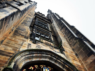 Gothic stone tower and stained glass entry of a historic New College in Edinburgh, Scotland, UK with dramatic upward perspective on weathered sandstone facade