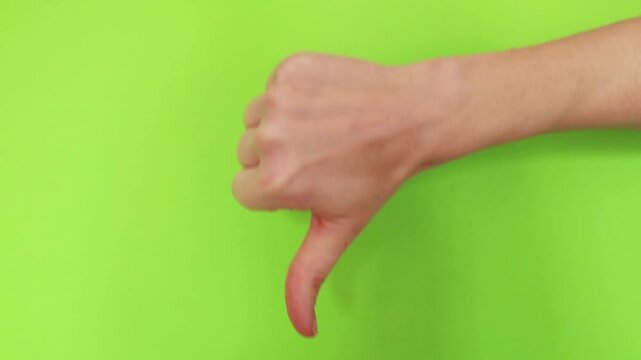 Close up of female hand showing thumbs down gesture on green background. Dislike symbol, negative feedback and rejection concept used in social media. Gesture isolated on chroma key