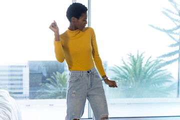 African American woman posing in bedroom by large window wearing mustard top, ripped jeans © wavebreak3