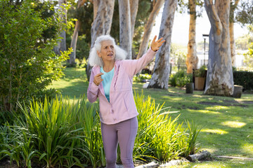Senior woman pointing and looking toward grasses in park wearing pink jacket and leggings © wavebreak3