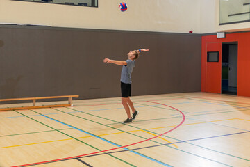 Male player serving red-and-blue volleyball in gym wearing gray tee and black shorts, copy space © wavebreak3