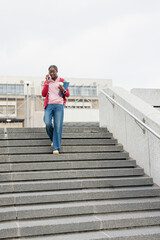 African American woman descending campus steps holding blue folder cup, speaking on phone near rail © wavebreak3
