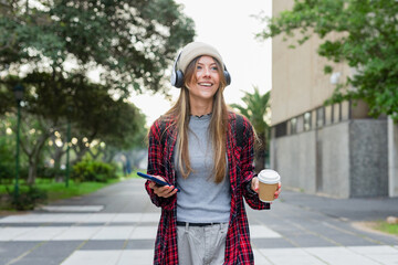 Woman walking along paved path beside modern building holding smartphone and coffee cup © wavebreak3