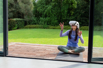 Woman sitting on yoga mat patio wearing lavender top white VR headset reaching, copy space © wavebreak3